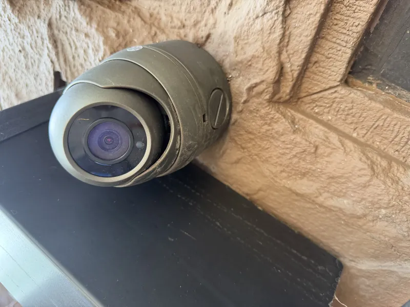 Weathered outdoor dome camera with dust and grime on its housing and lens cover, mounted on a textured exterior wall