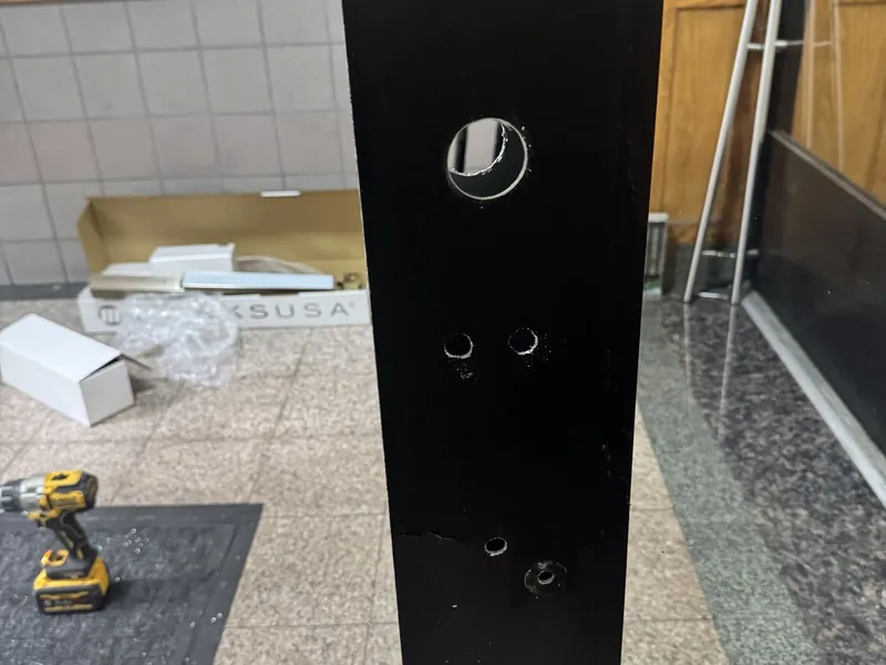Edge of a black entrance door stile with the hardware removed, showing its mounting holes