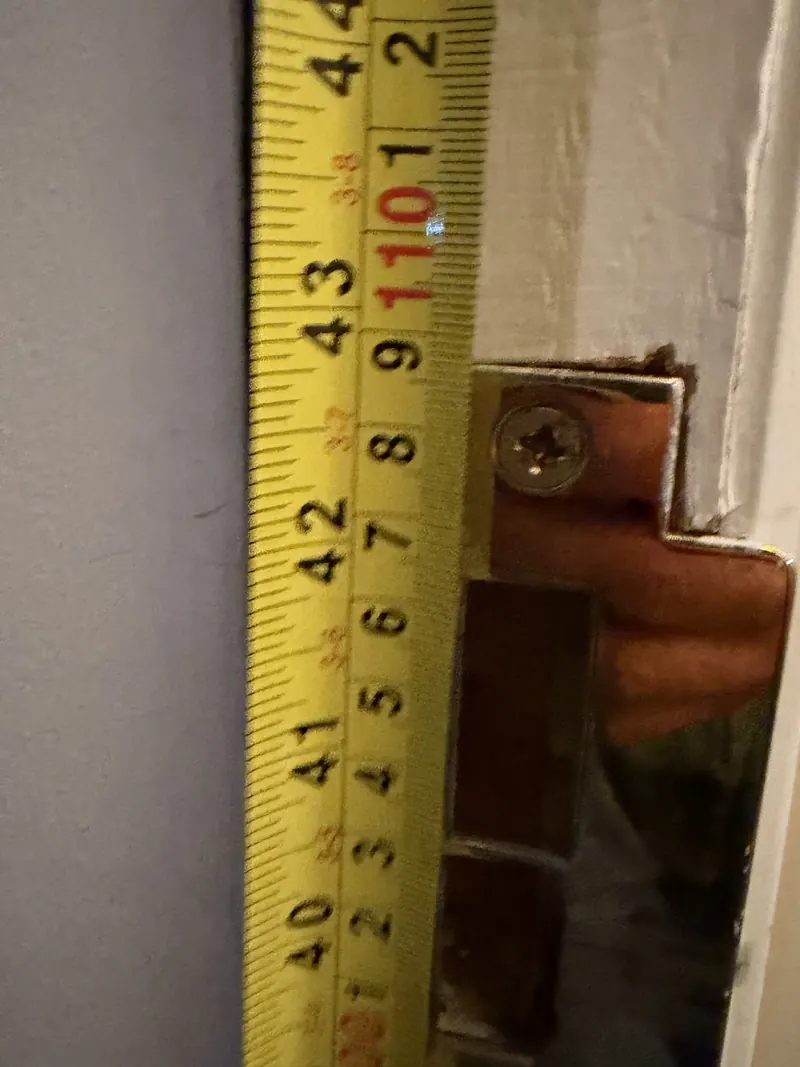 Tape measure held against a door frame next to a brass strike plate during a door inspection