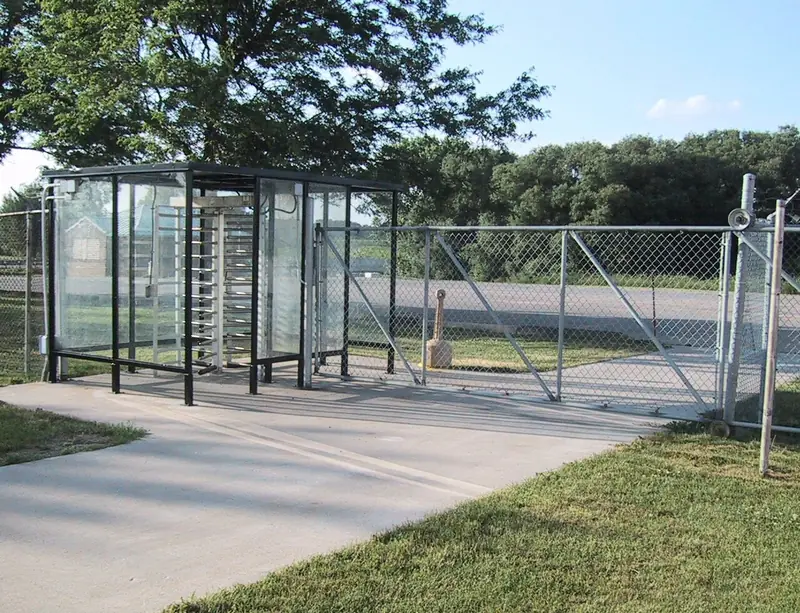 Turnstile enclosure beside a chain-link gate at a fenced entrance