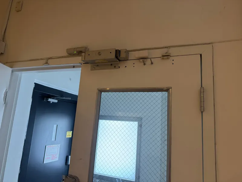 Magnetic lock mounted on the head of a door frame above a door with wired glass, with door position switches nearby
