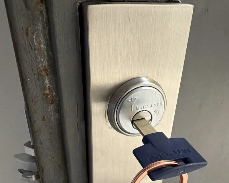 High-security key cylinder in the escutcheon of a mortise lock on a steel entrance door, with a key inserted