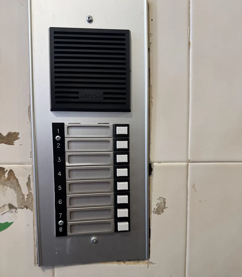 Eight-button apartment building audio intercom panel with blank name labels, mounted on a tiled entrance wall