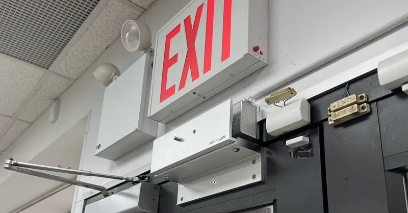 Magnetic lock, door position switches and an overhead door closer mounted above a glass entrance door beneath an illuminated exit sign