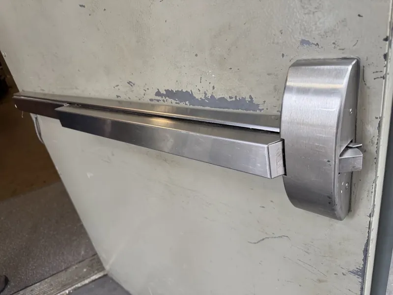 Older metal rim exit device with a rounded latch housing on a worn painted door