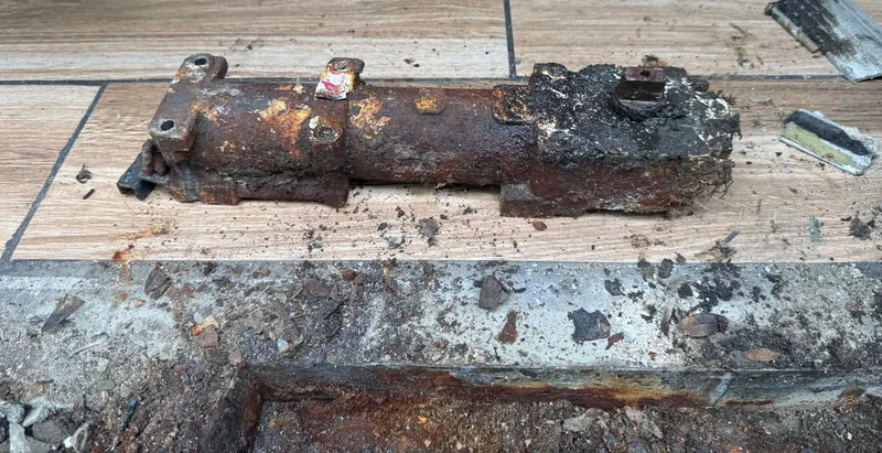A rusted-through storefront floor closer removed from its pit, next to a corroded metal threshold at a shop entrance