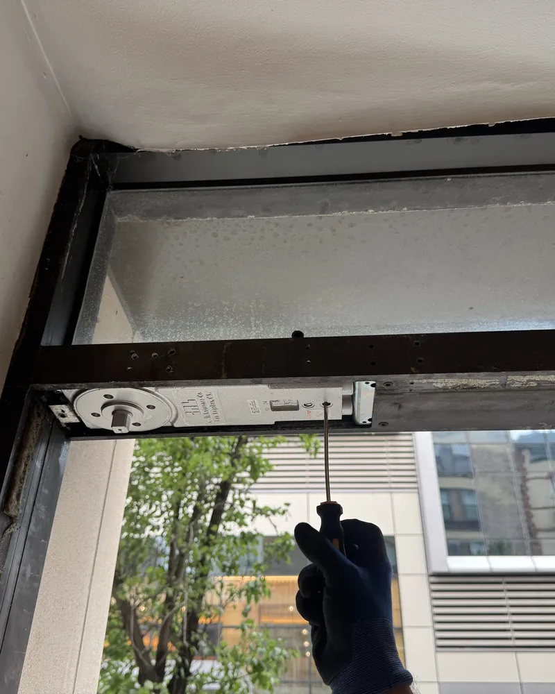 Technician adjusting a concealed overhead closer in the header of an aluminum storefront door with a screwdriver