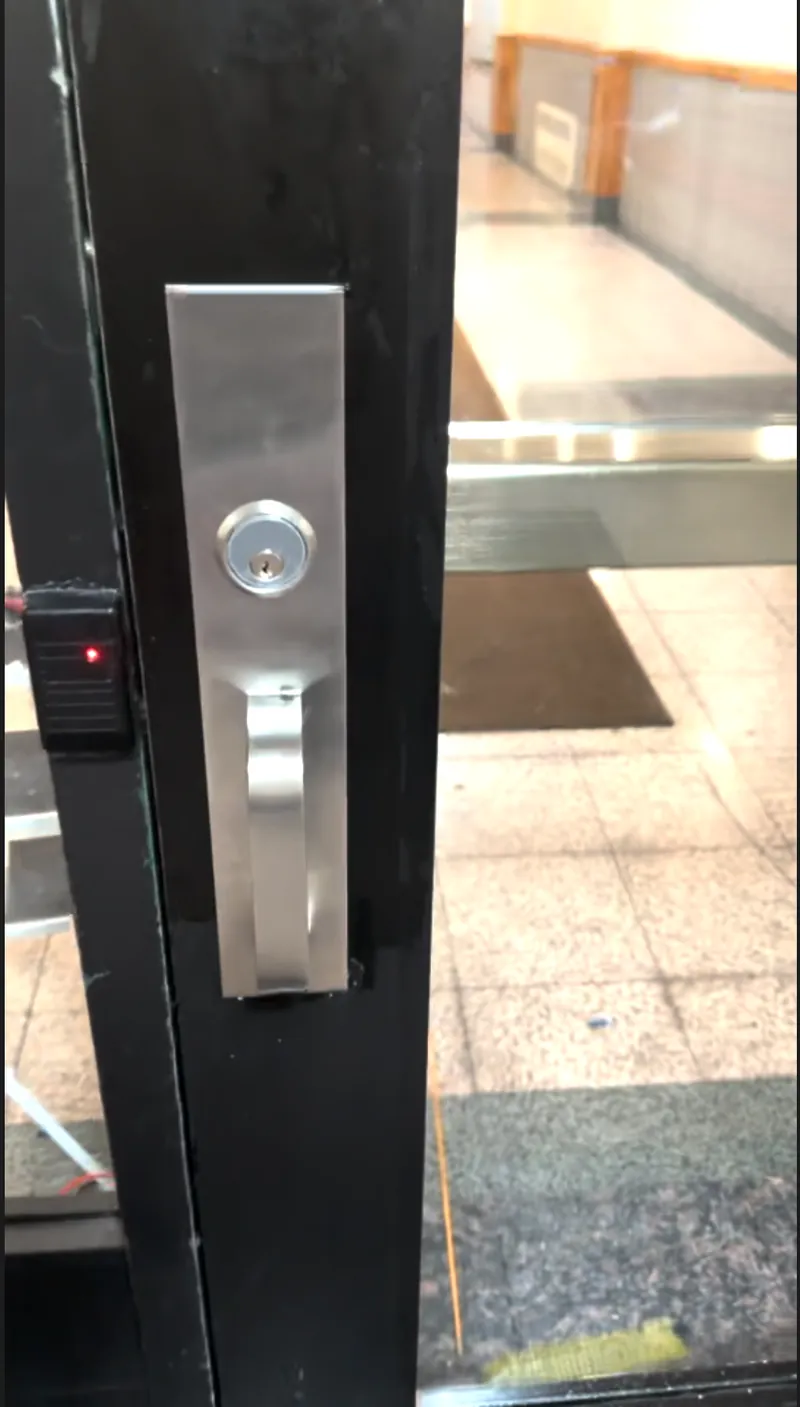 Key cylinder and lever trim on the edge of a black aluminum entrance door