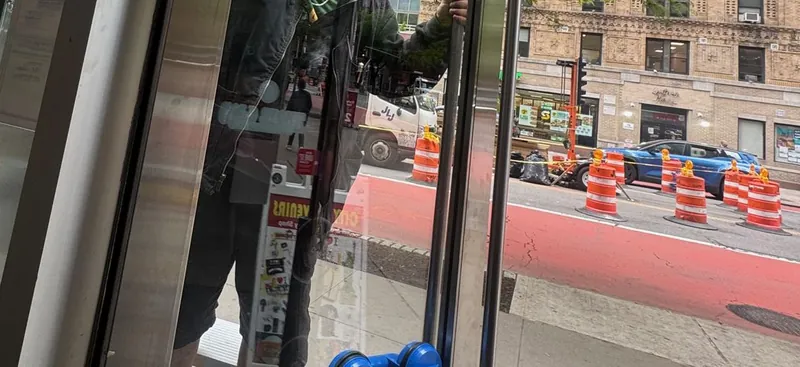 A glass storefront door being lifted off with suction-cup handles, seen from inside the shop