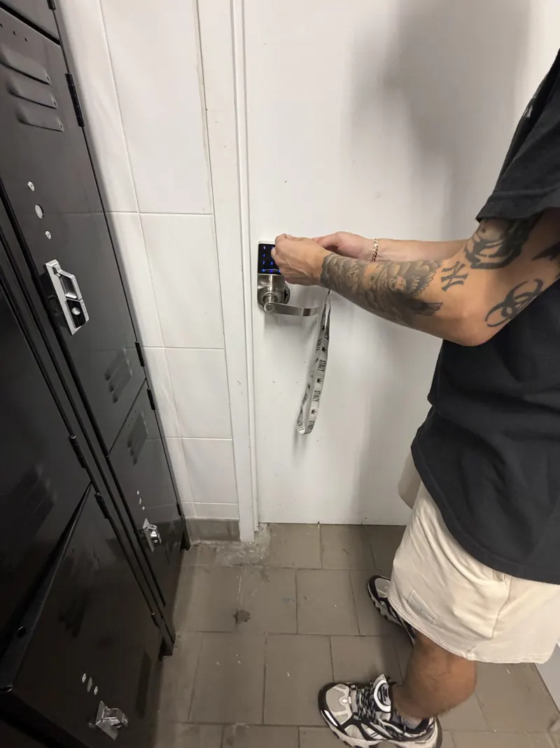 Technician installing a keypad lever lock on a white door beside a row of lockers