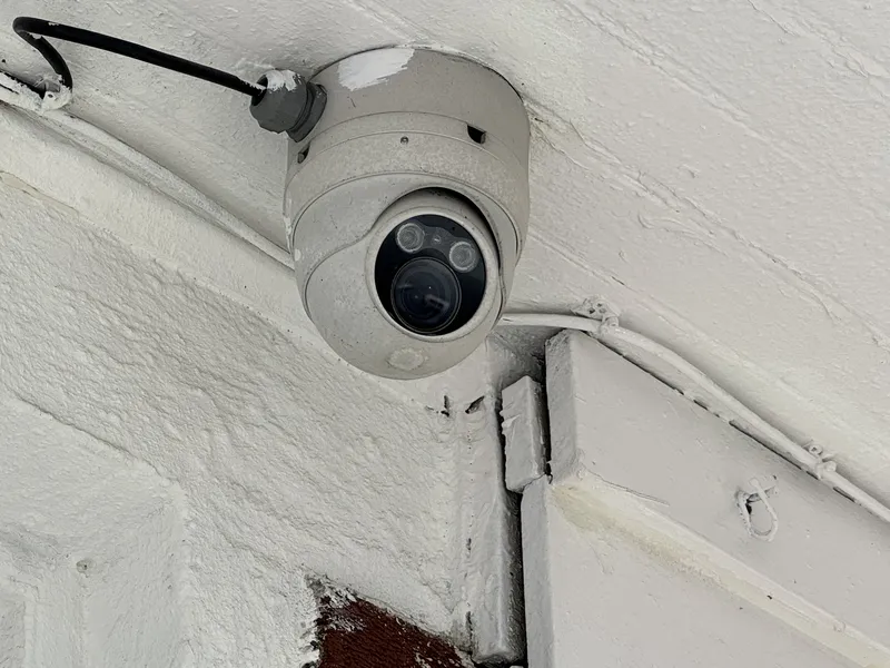 Outdoor turret security camera with two infrared illuminators, mounted under a painted building overhang