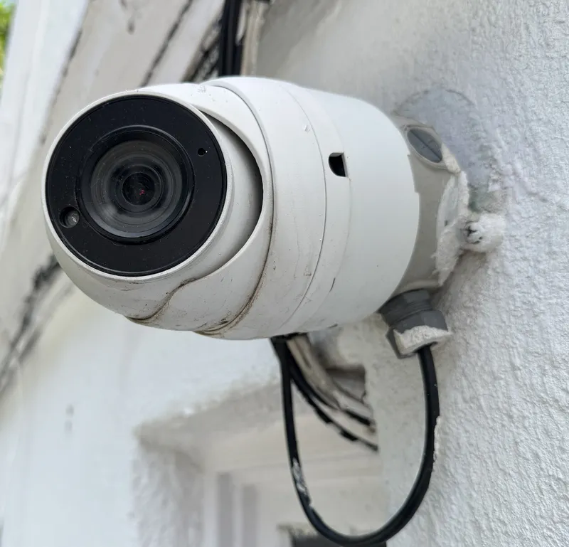 White turret camera on an exterior wall, with its cable entering a weatherproof junction box behind the camera
