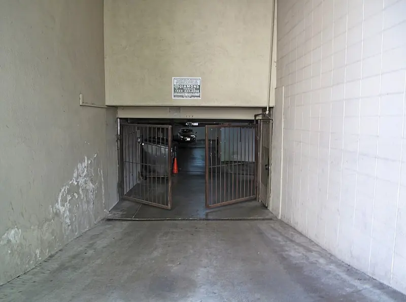 Two-leaf metal gate partly open at the bottom of an underground garage ramp
