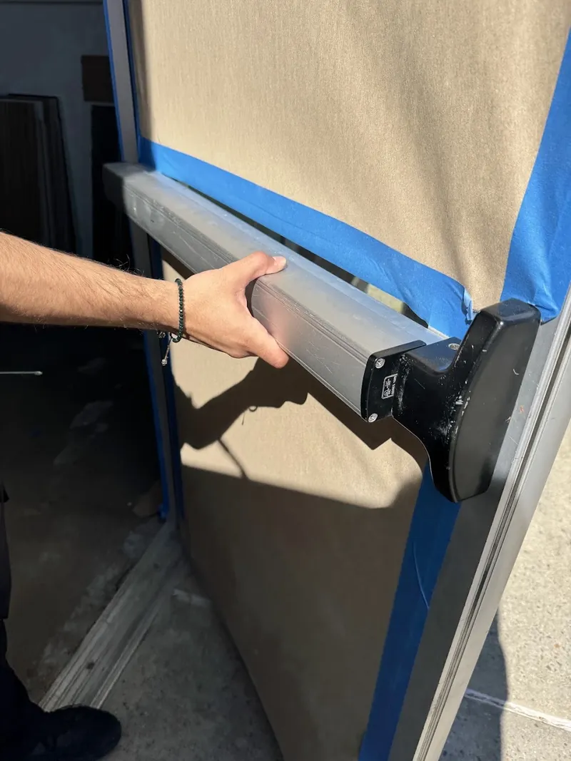 Hand operating a Von Duprin push pad during installation on a door covered with protective paper and blue tape